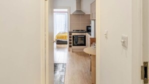 A narrow hallway leading to a kitchen with a stove, microwave, and cabinets. - Springfield - The Earl (London)