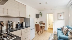 A modern kitchen with a dining area, a blue sofa, and a TV mounted on the wall. - Springfield - The Earl (London)