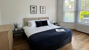 Une chambre à coucher comprenant un lit, des tables de chevet, une commode et une fenêtre avec des stores.