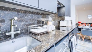 Une cuisine moderne dotée d’un plan de travail en marbre, d’un évier en acier inoxydable et d’appareils électroménagers intégrés.