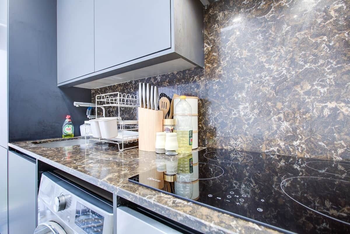 A kitchen with a black countertop, a dish rack, and various kitchen utensils.