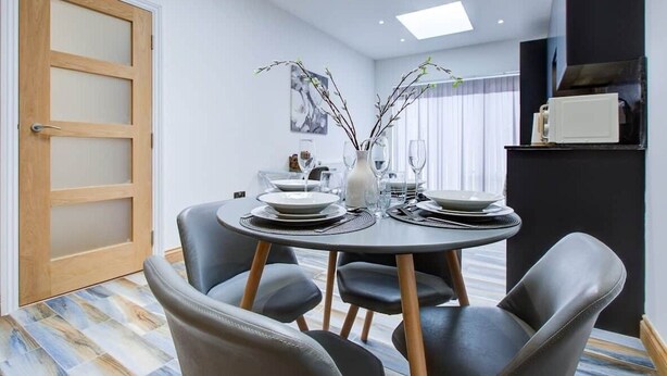 Un espace repas moderne avec une table ronde, des chaises grises et une porte en bois.