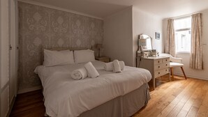 Une chambre à coucher avec un grand lit, une commode, un miroir et une fenêtre avec des rideaux.