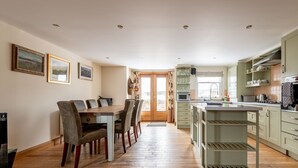 A spacious kitchen with wooden flooring, a dining area with a table and chairs, and a view through a door to the outside. - Golf Court (No 2) | Elie (Elie)