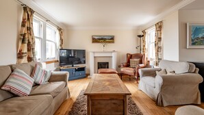 A living room with a sofa, armchairs, a coffee table, a fireplace, and a television. - Golf Court (No 2) | Elie (Elie)