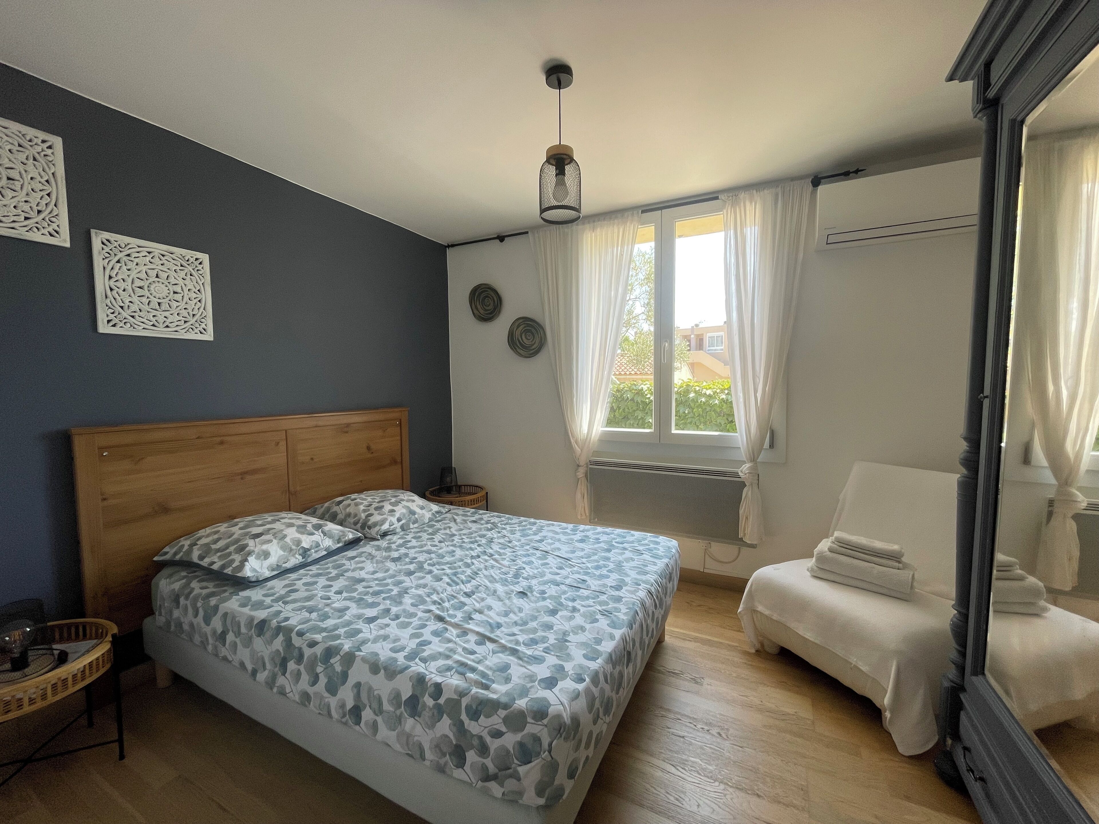 Un dormitorio con una cama de cabecera de madera, una mesita de noche, una silla y una ventana con cortinas.
