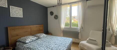 Un dormitorio con una cama de cabecera de madera, una mesita de noche, una silla y una ventana con cortinas.