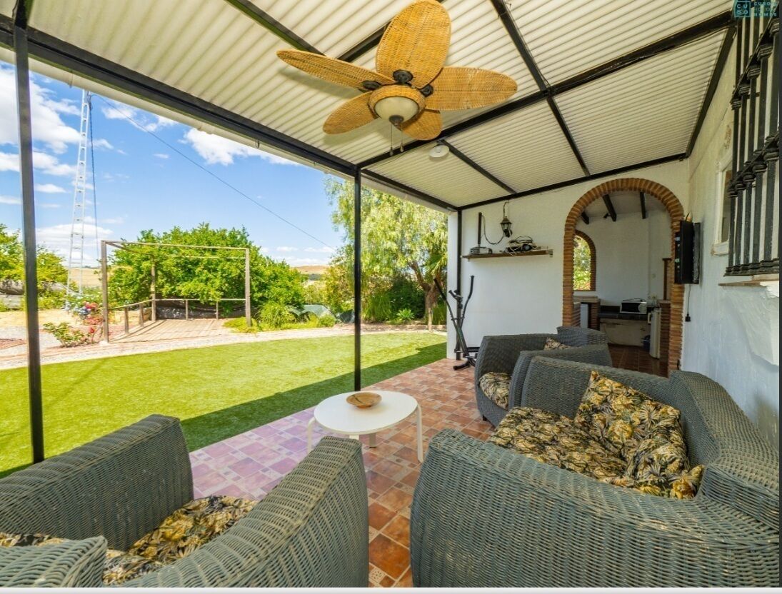 Un portico coperto con mobili in vimini, una ventola a soffitto e vista sul giardino.