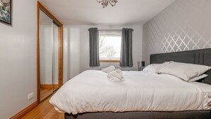 Ein Schlafzimmer mit einem Bett, einem Fenster mit Vorhängen, einer Deckenleuchte und einem Spiegel.