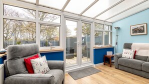 Ein Wintergarten mit Glastür zum Garten, ein graues Sofa mit roten Kissen, ein kleiner Tisch mit Lampe und eine blaue Wand.