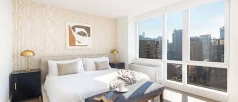A modern bedroom with a large bed, bedside tables, a bench, and a city view through large windows.