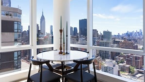 Een hoog gelegen kamer met een groot raam en uitzicht op de stad, een ronde tafel met stoelen en een decoratieve vaas.