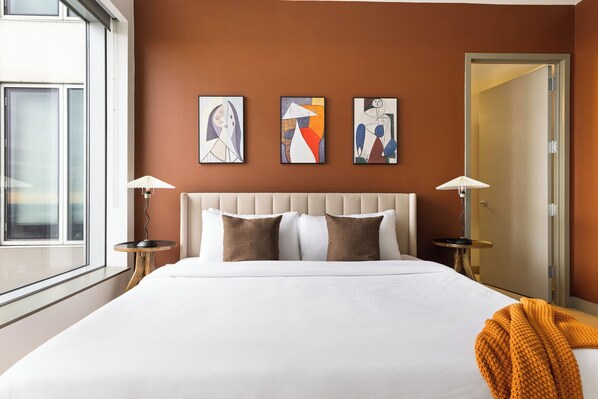 Una habitación de hotel con una cama grande, dos mesitas de noche, un ventanal y arte abstracto en la pared.