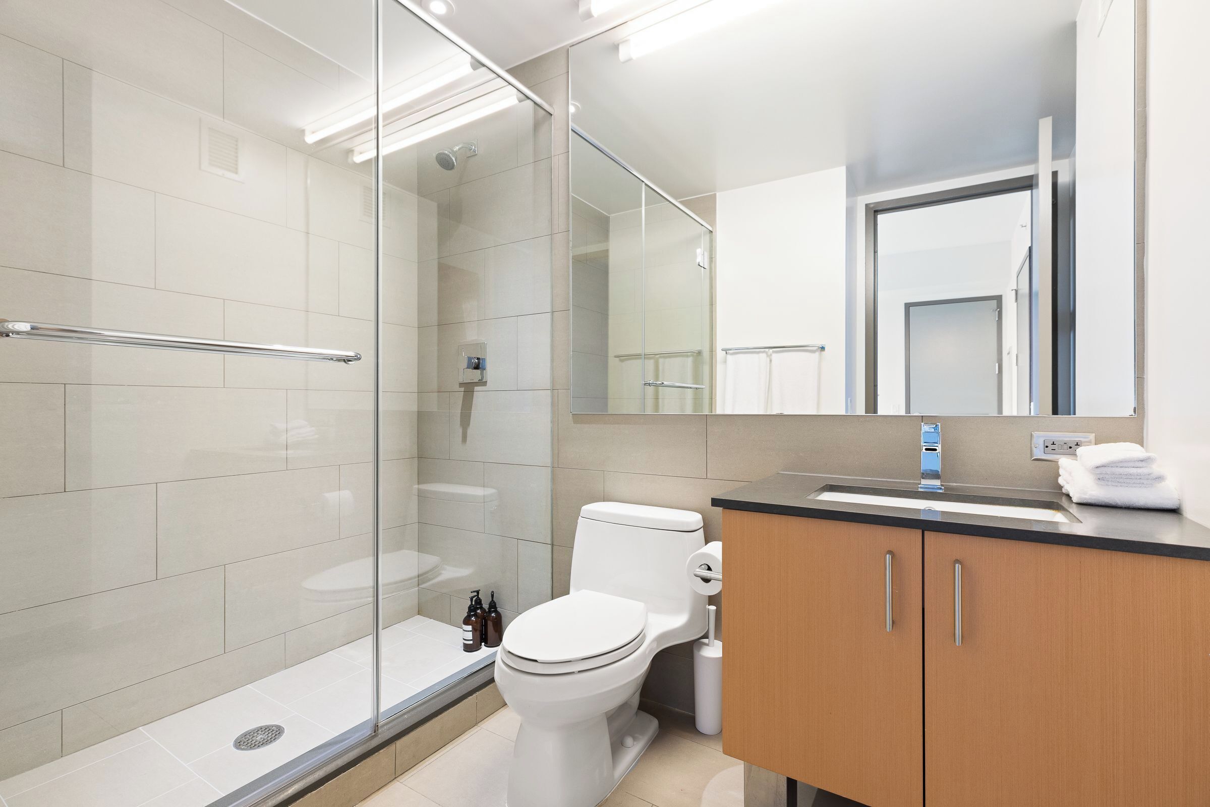 A modern bathroom with a glass-enclosed shower, a toilet, and a wooden vanity with a sink.