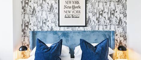 A hotel room with a cityscape wallpaper, a blue headboard, and two bedside lamps.