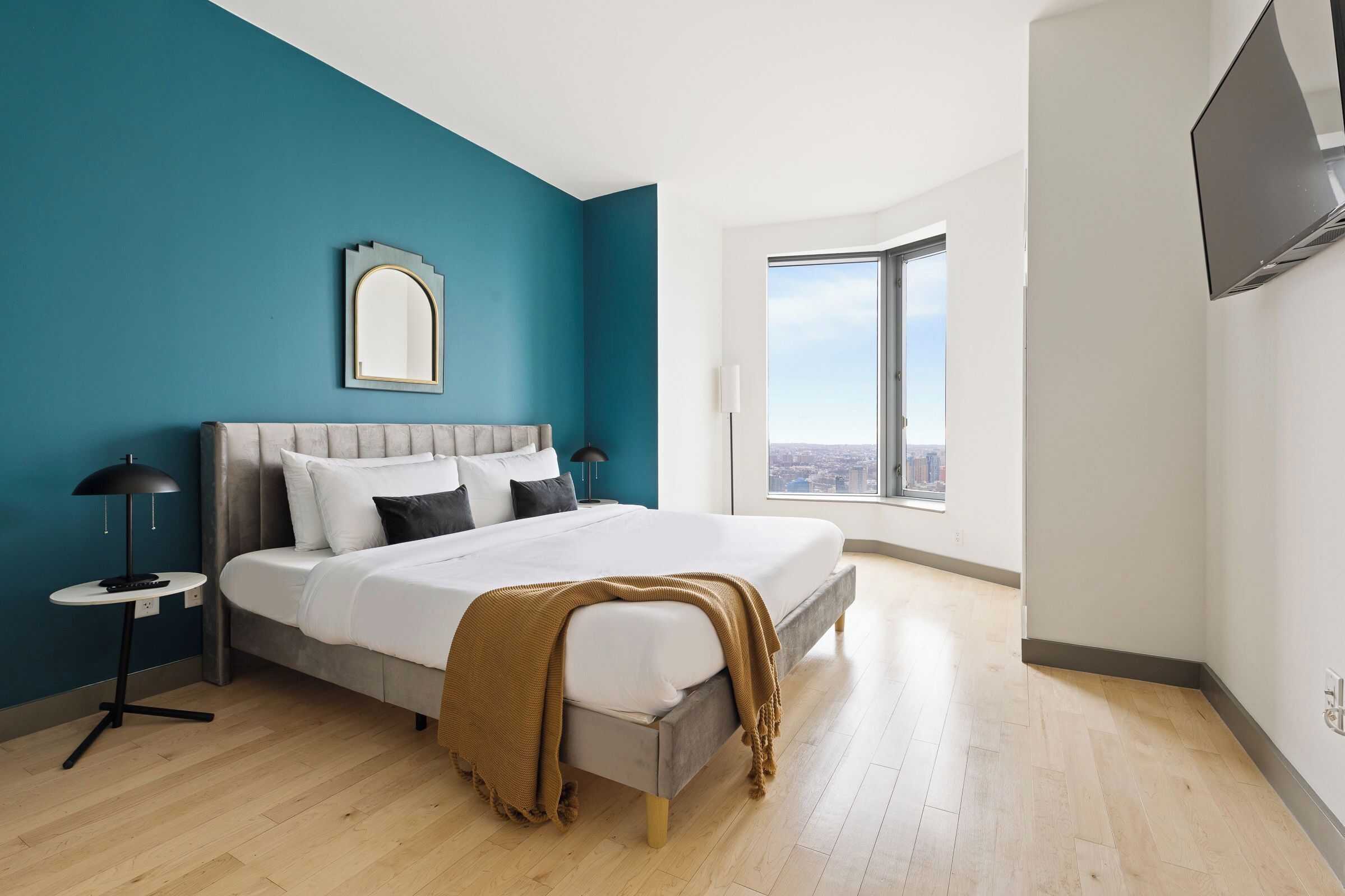 Ein modernes Schlafzimmer mit einem großen Bett, Blick auf die Stadt und einem an der Wand montierten Fernseher.