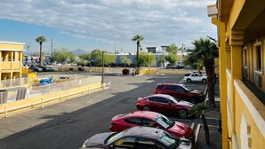 Un parking avec plusieurs voitures, un bâtiment jaune et des palmiers en arrière-plan.