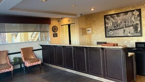 Un espace d’accueil avec un comptoir, des meubles en bois foncé, deux chaises à motifs, une horloge et un panneau encadré accroché au mur.
