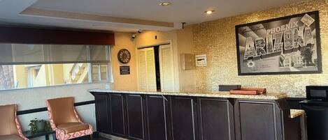 A reception area with a counter, dark wooden cabinets, two patterned chairs, a clock, and a framed sign on the wall.