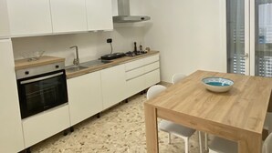 Une cuisine moderne avec des meubles blancs, un four encastré, une cuisinière à gaz et une table à manger en bois avec des chaises.