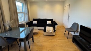 Un salon moderne avec une table à manger en verre, un canapé noir et un fauteuil gris.