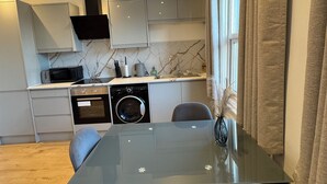 Une cuisine moderne dotée d’appareils électroménagers intégrés, un coin repas avec une table en verre et une vue sur l’extérieur.