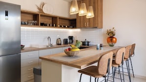 Una cocina moderna con refrigerador de acero inoxidable, armarios de madera, una isla central con taburetes de bar e iluminación colgante.