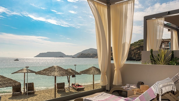 Un balcón frente a la playa con vista al mar, una silla de lounge y una mesa con una manta.