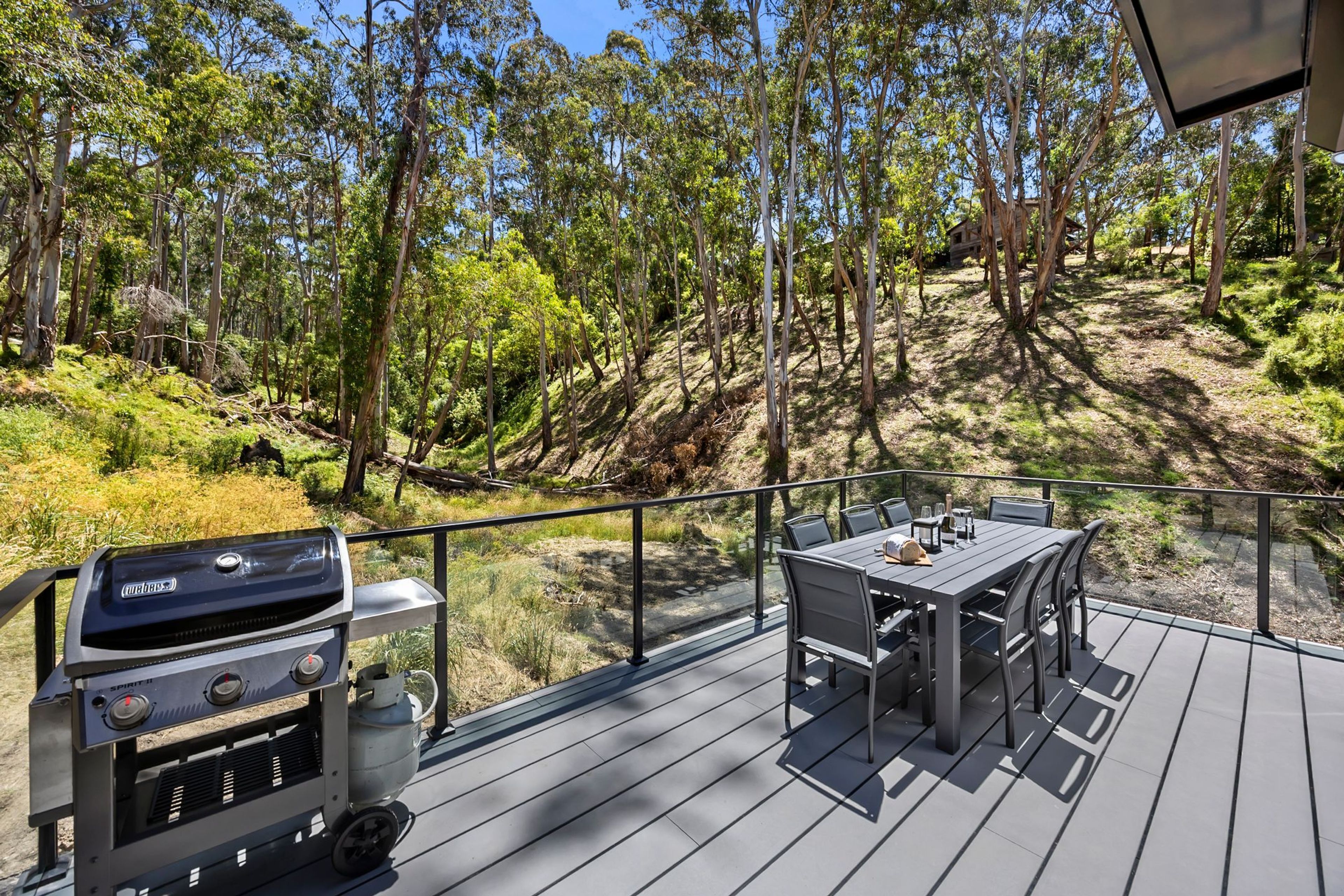An outdoor deck with a grill and dining area overlooking a forested hillside.