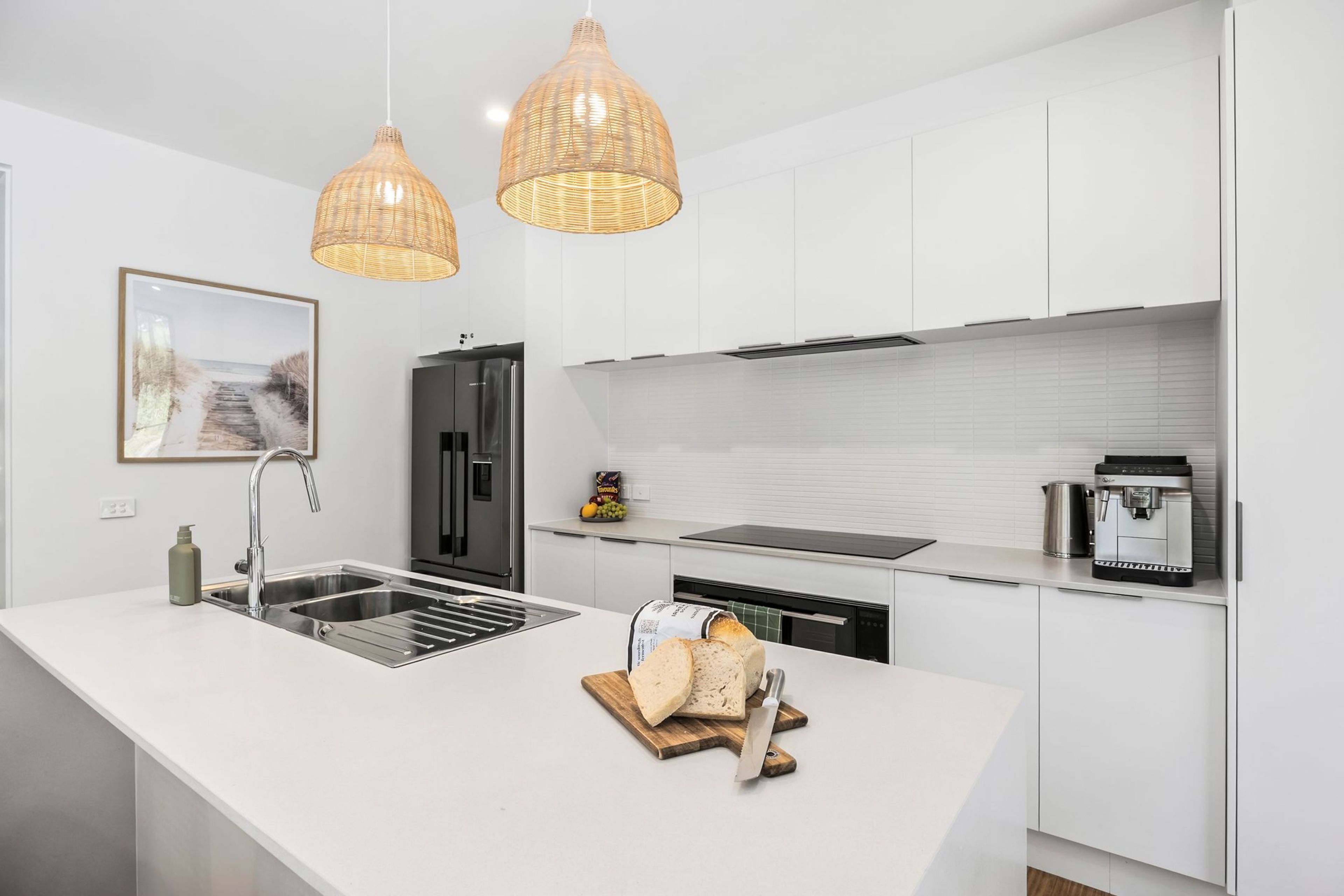 A modern kitchen with a white island, stainless steel appliances, and wicker pendant lighting.