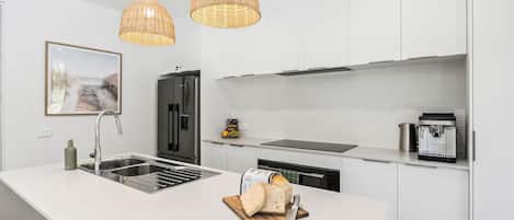 A modern kitchen with a white island, stainless steel appliances, and wicker pendant lighting.
