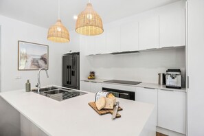 A modern kitchen with a white island, stainless steel appliances, and wicker pendant lighting. - Sea North (Lorne)