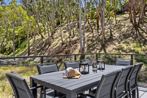 An outdoor dining area with a table set for two, surrounded by chairs, with a bottle of wine and a loaf of bread on the table. - Sea North (Lorne)