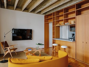 Ein modernes Wohnzimmer mit einer Couch, einem Couchtisch, einem Fernseher und einer Küchenzeile mit Holzschränken und einer Mikrowelle.