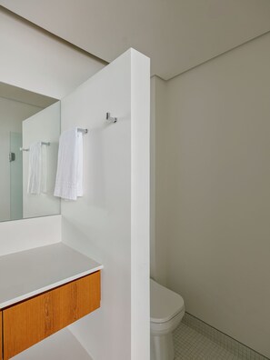 A modern bathroom with a white vanity, a mirror, a toilet, and a shower area. - 2217B (São Paulo)
