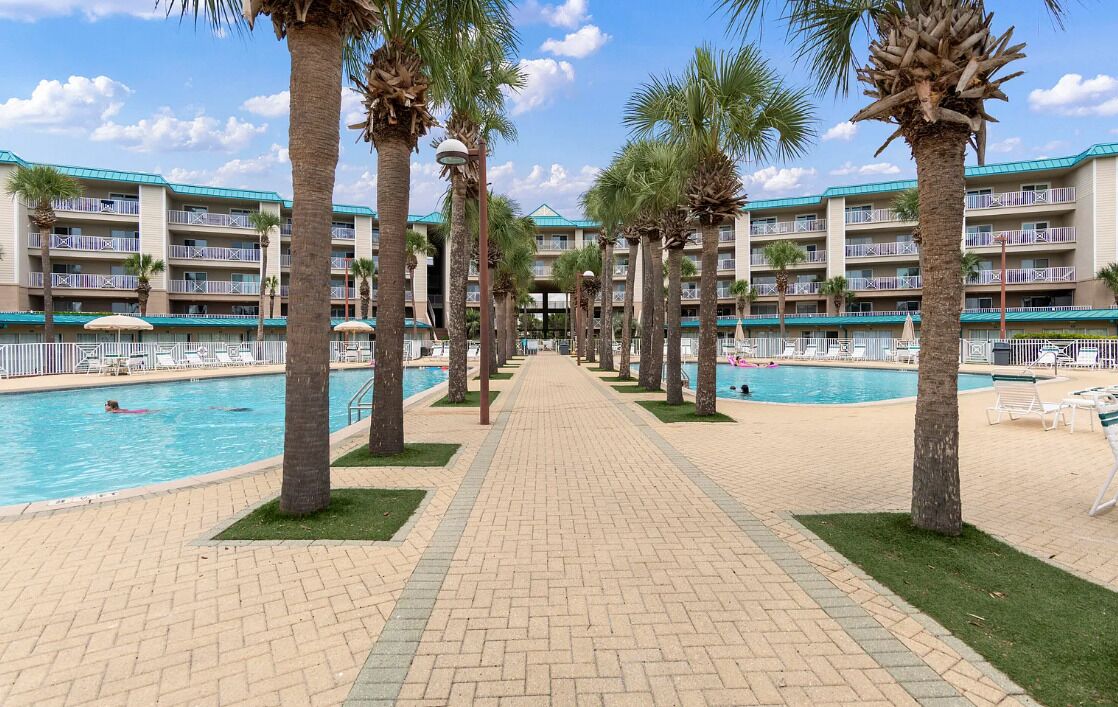 A hotel with a pool area, palm trees, and a brick pathway.