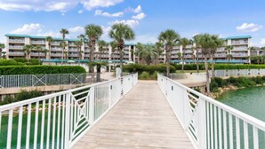 Un puente de madera que lleva a un hotel con varios balcones y palmeras.