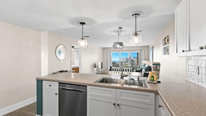Une cuisine moderne dotée d’un îlot central, d’appareils électroménagers en acier inoxydable et de luminaires suspendus.