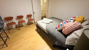 A bedroom with a bed, a chair, a small table, and a door leading to a bathroom. - Brixton Bright Apartment (London)