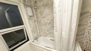 A bathroom with a bathtub, a window, and a shower. - Brixton Bright Apartment (London)