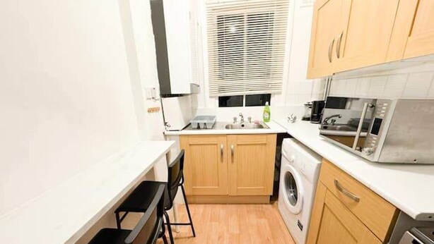 A compact kitchen with wooden cabinets, a washing machine, a microwave, and a sink. - Brixton Bright Apartment (London)