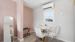A room with a round table, two chairs, a small potted plant, a window, and an air conditioning unit. - Pink Champagne Boutique Motel (Wildwood)