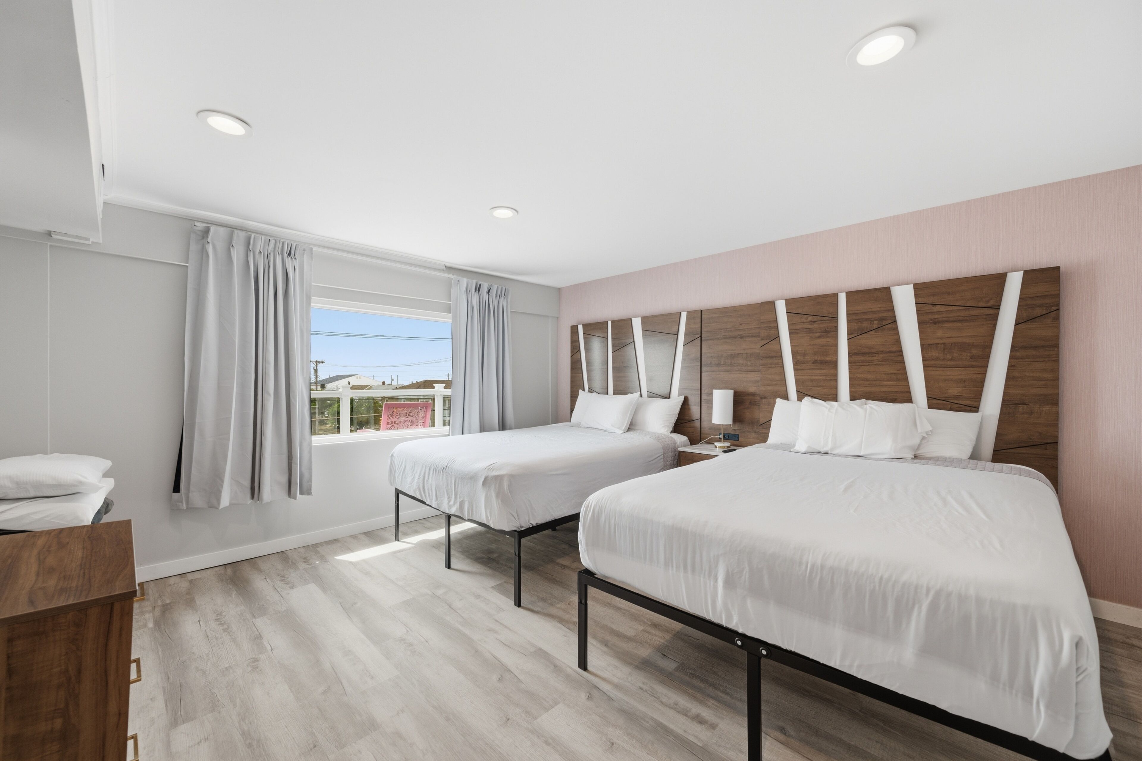 Un dormitorio con dos camas, un aparador de madera, una ventana con cortinas y un cabecero fijado a la pared.