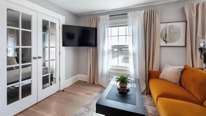 Un salon avec un canapé, une table basse ornée d’une plante, un téléviseur et une fenêtre avec des rideaux.