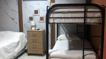 A dormitory room with two bunk beds, a bedside table with a lamp, and a wall-mounted air conditioner.
