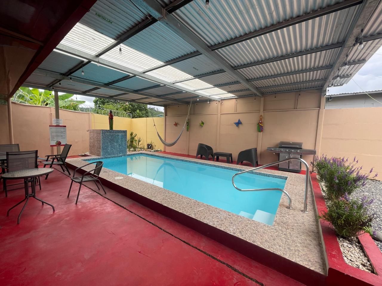 Una piscina interior con suelo rojo, rodeada de sillas y una parrilla.