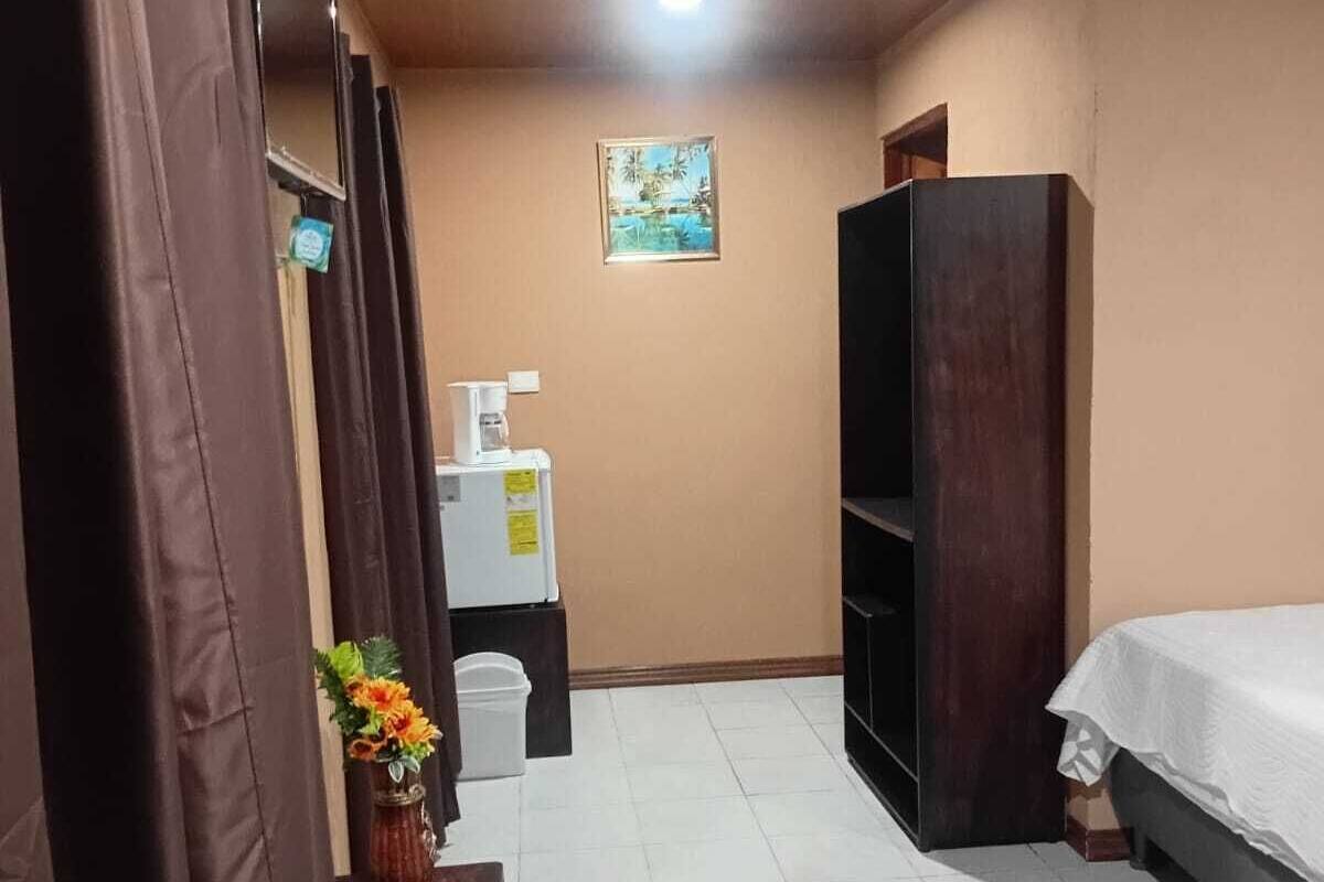 Egy szállodai szoba, amelyben található egy ágy, egy kis asztal egy kávéfőzővel, egy szemeteskosár, egy szekrény és egy kép a falon.