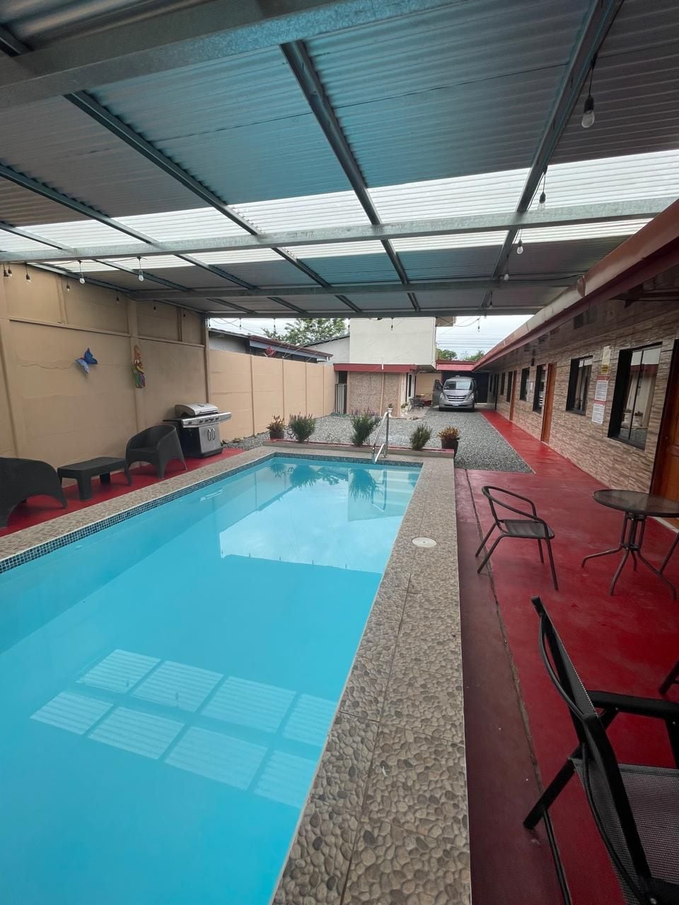 A swimming pool with a covered area, outdoor seating, and a vehicle in the background.