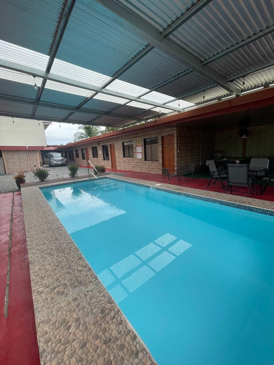 A swimming pool with a covered area, a red pathway, and a building with a red roof and stone walls.