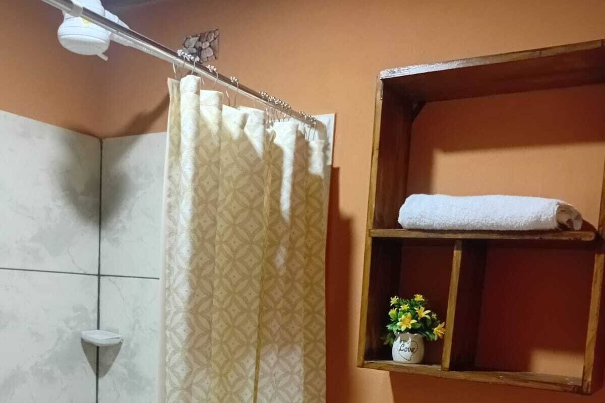 Egy fürdőszoba zuhanyzóval, WC-vel, mosdókagylóval, valamint egy polccal, amelyen törölköző és virágok találhatók.